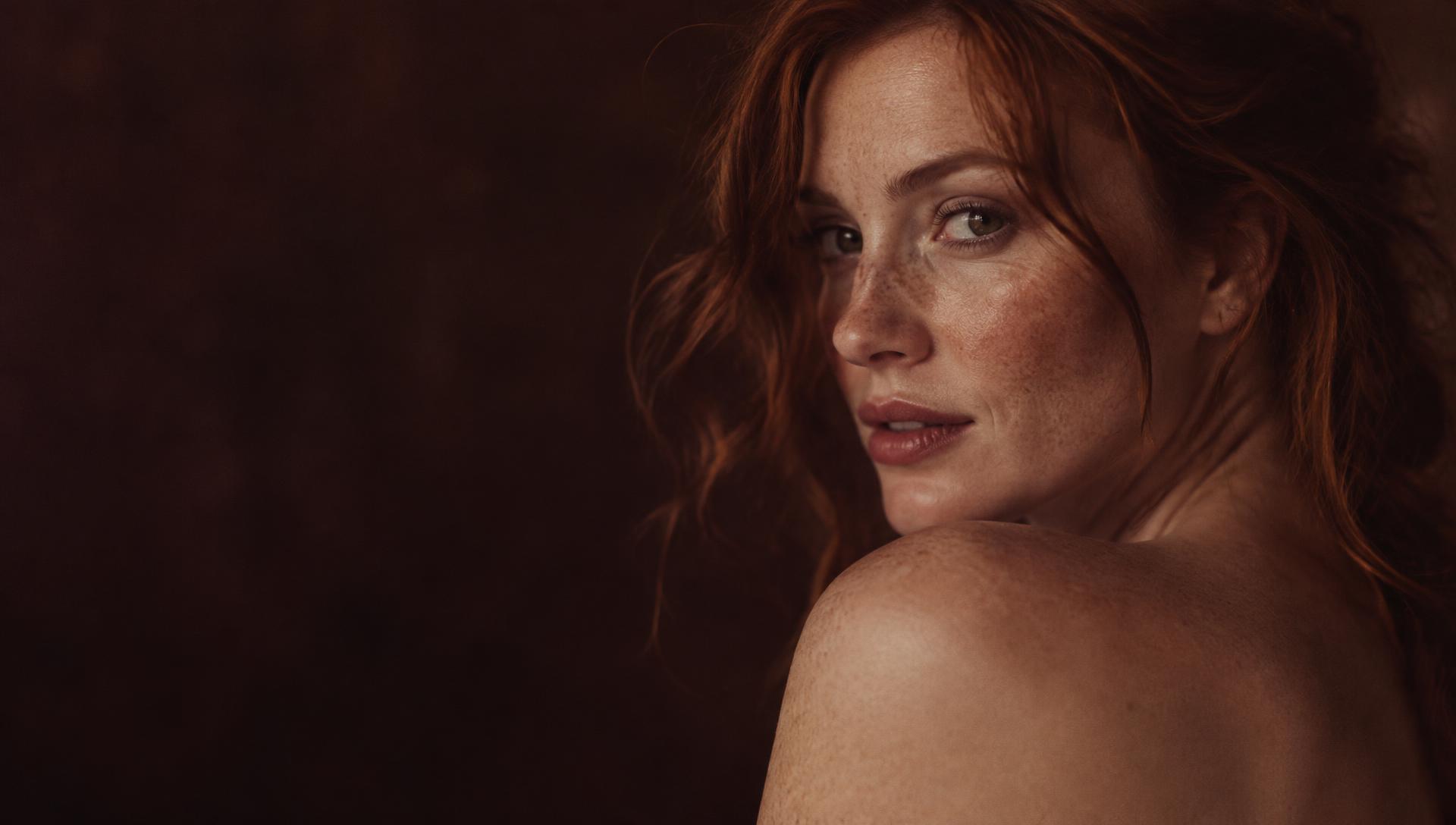Freckled woman looking over her bare shoulder