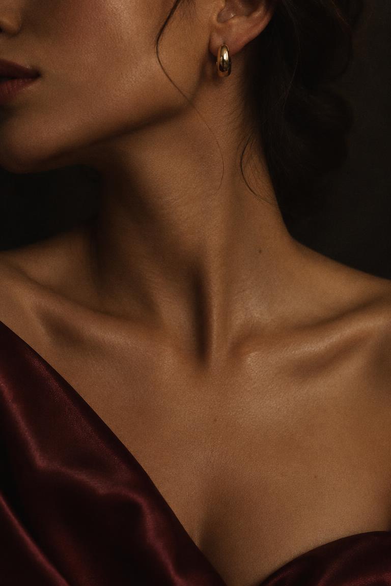 Close up of a woman's neck and collarbone with a gold earring